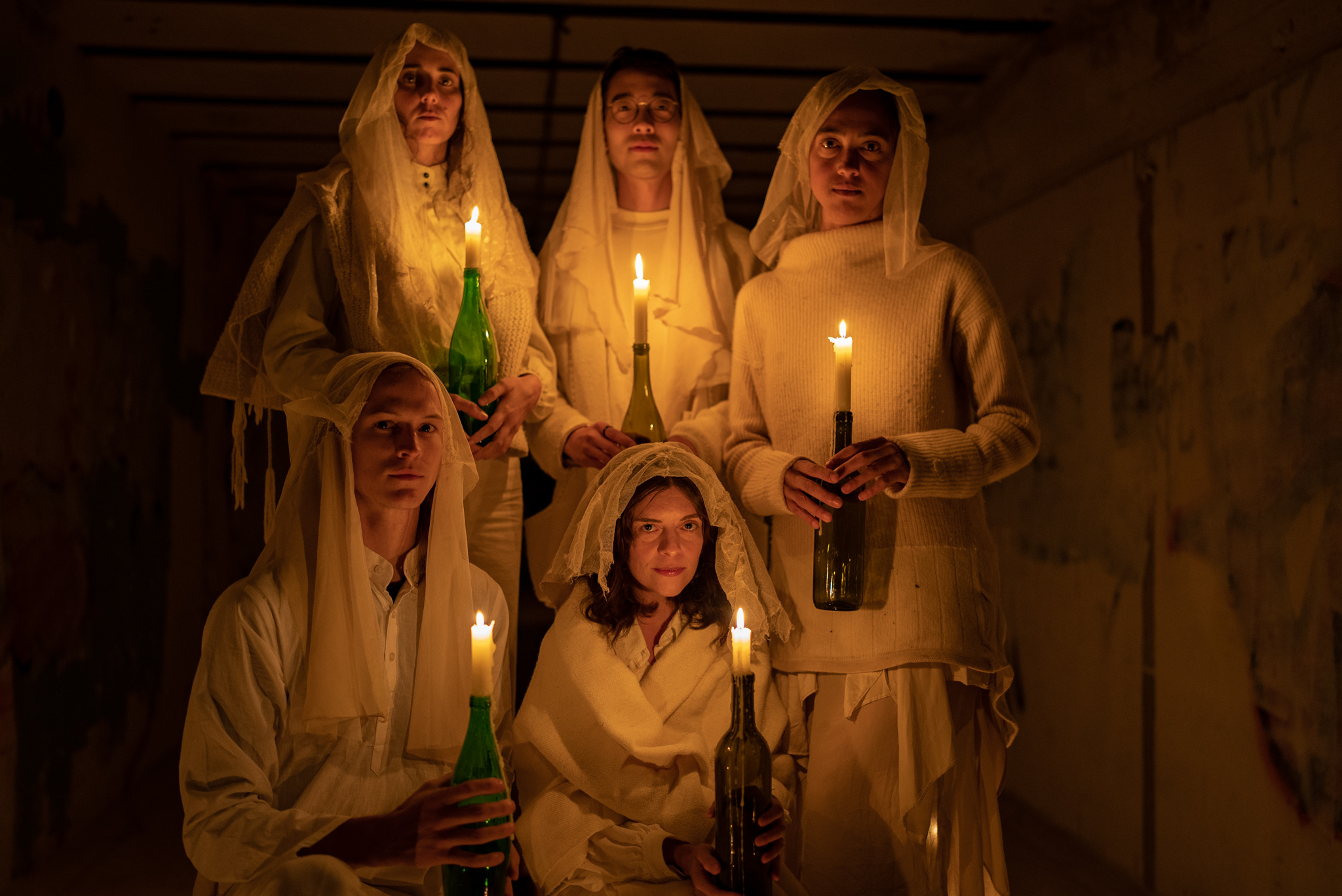 Five performers holding candles inside bunker space