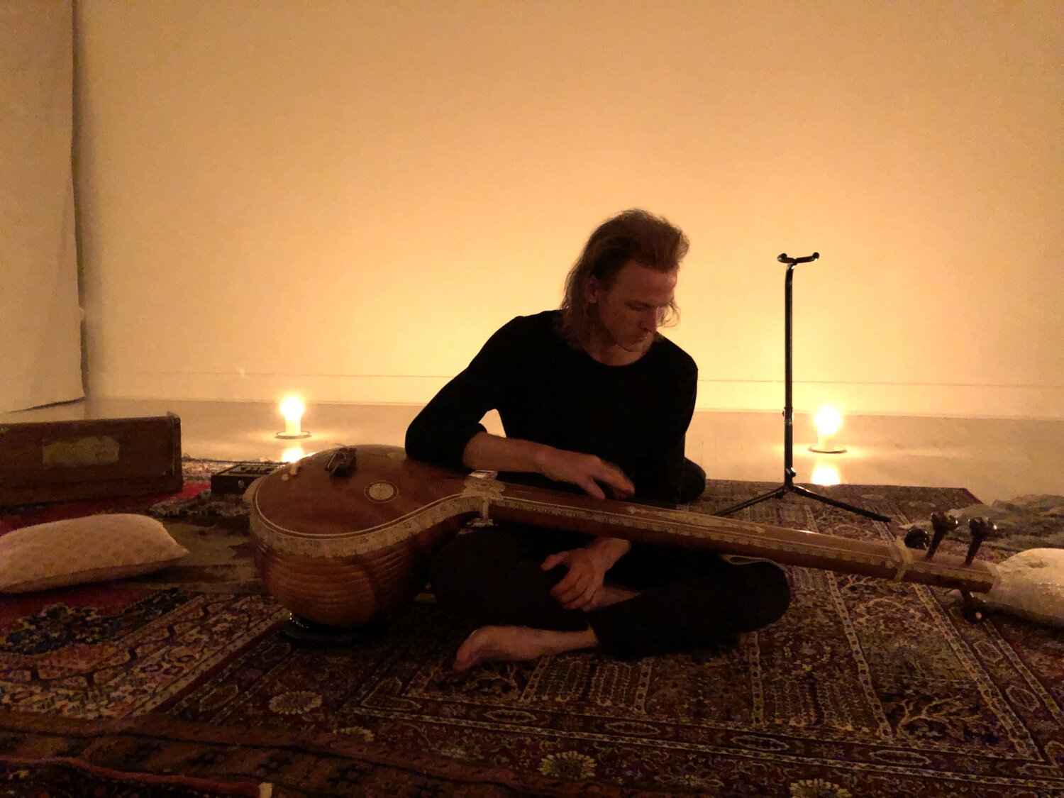 a candlelit room of rugs and Joey tuning a tambura